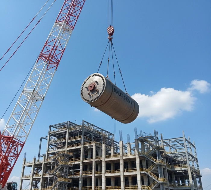 Lifting heavy components using a crane at the PLTU construction site.